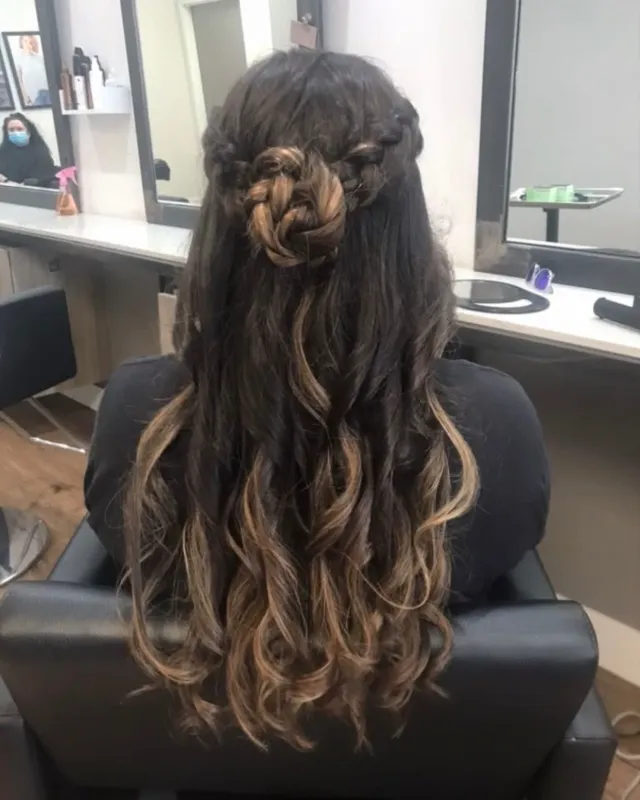 Half-up hairstyle with braided floral detail and curled blonde lengths.